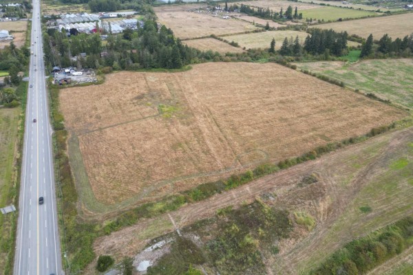 Wide aerial view showing a rural landscape with a highway, fields, and wooded areas. - 17690 12 Avenue, Surrey