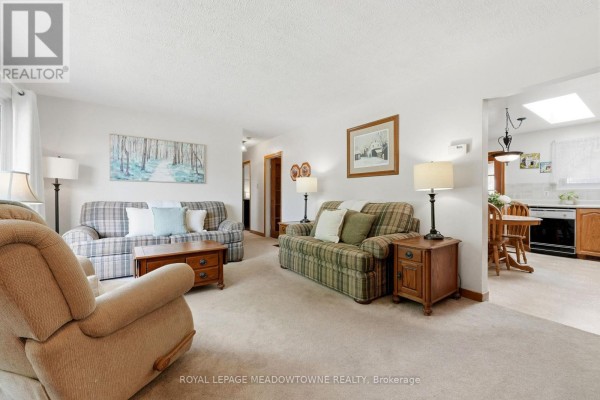 Living room with beige carpet, two plaid sofas, a recliner, wooden coffee table, and view to dining area. - 177 Delrex Boulevard, Halton Hills