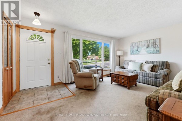 Entrance of the living room with a white front door, tiled entryway, plaid sofa, recliner, and large window. - 177 Delrex Boulevard, Halton Hills