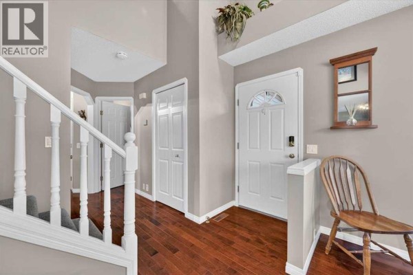 Interior foyer with dark hardwood floors, a white staircase, and multiple doors. - 177 Douglasview Rise Se, Calgary