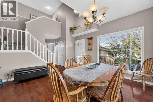 Dining room with a wood table, chairs, and a large window overlooking the street. - 177 Douglasview Rise Se, Calgary