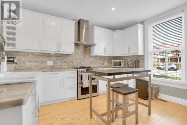 Kitchen with white cabinets, stainless steel appliances, stone backsplash, and island with stools. - 177 Dunlop Street W, Barrie