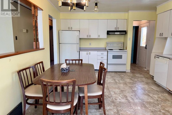 Dining area with a wooden table and chairs, adjacent to a kitchen with white appliances. - 177 Georgina Avenue, Temiskaming Shores