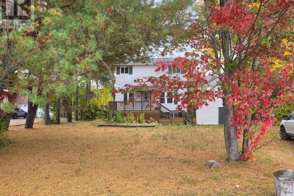 Front view of a light gray house with a deck, surrounded by trees with fall foliage. - 177 River Rd, Sault Ste  Marie