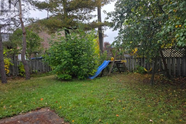Backyard with a wooden fence, a blue slide, a swing set, and green grass. - 177 River Rd, Sault Ste  Marie