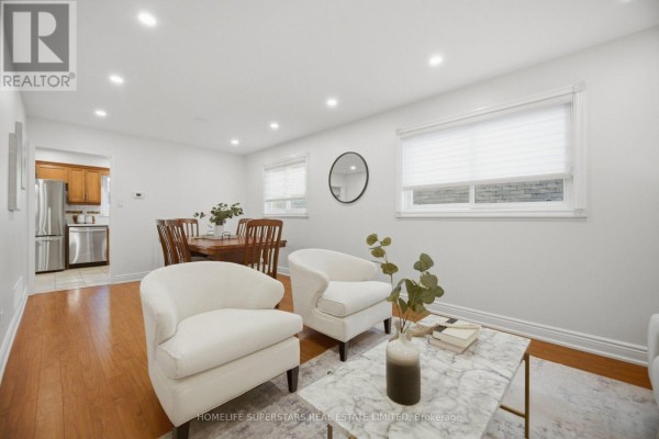 Living and dining area with two white armchairs, a marble coffee table, and a wooden dining set visible. - 177 Surbray Grove, Mississauga