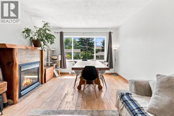 Living room and dining area with fireplace, large dining table, and view of trees. - 1771 Harris Road, Squamish