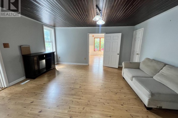 Living room with light wood floors, dark wood plank ceiling, and an open doorway. - 1773 20th Side Road, Innisfil