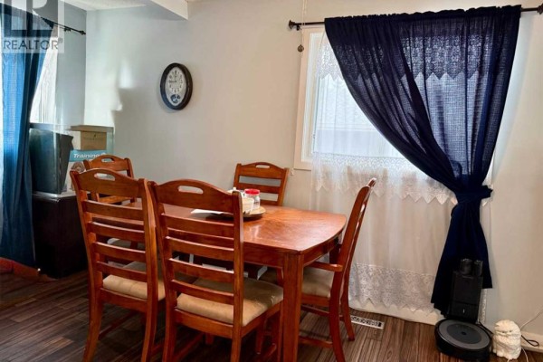 Dining area with a wooden table and four chairs, dark blue and white curtains, and dark wood flooring. - 178 Hansen Drive, Hinton