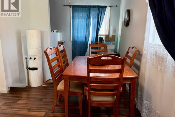 Dining room with a wooden table set for four, water cooler, and dark blue curtains on the right. - 178 Hansen Drive, Hinton