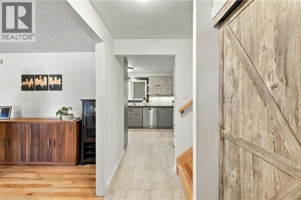 Interior hallway with light tile floors, a barn door, and a view into the grey-toned kitchen. - 178 Laurentian Drive, Kitchener