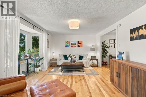 Living room with a bay window, light wood floors, white walls, a sofa, and a leather ottoman. - 178 Laurentian Drive, Kitchener