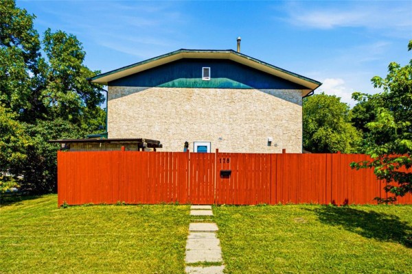 Front view of a two-story house with beige stone and green trim, enclosed by a bright orange fence. - 178 Pentland Street, Winnipeg