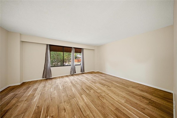 Empty room with light beige walls and polished hardwood floors, featuring three large windows. - 178 Pentland Street, Winnipeg