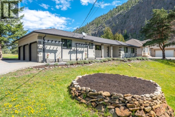 View of a beige stucco house with a large front lawn and mature trees. - 178 Range Road, Kaleden