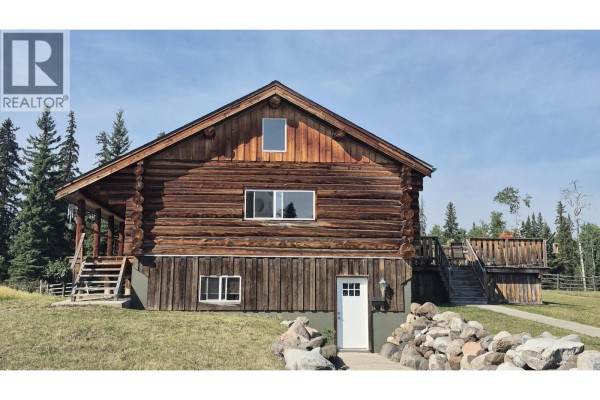 Wooden log home exterior with large windows, a walk-out basement door, and stone landscaping. - 17849 Langston Road, Vanderhoof