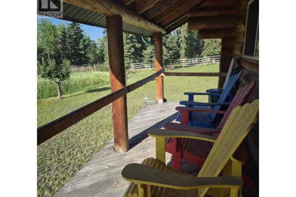 Close-up of colorful Adirondack chairs on a wooden porch overlooking a grassy yard and trees. - 17849 Langston Road, Vanderhoof