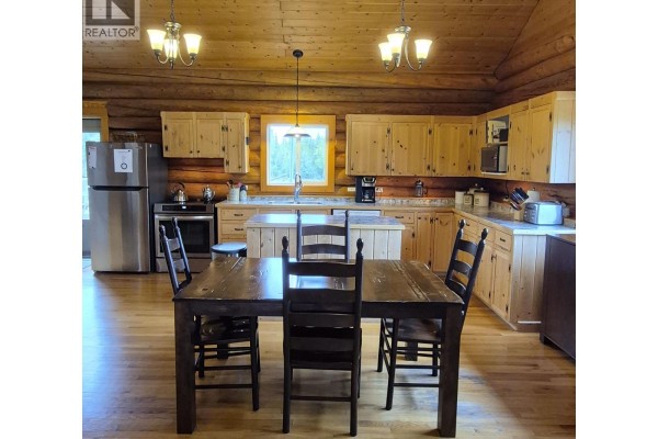 Kitchen and dining area with a dark wood table and chairs, light wood cabinets, and wood-paneled walls. - 17849 Langston Road, Vanderhoof