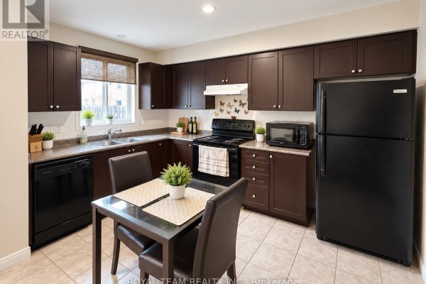 Kitchen with dark brown cabinets, black appliances, beige tiled floor, and a small dining table. - 1786 Swan Street, Innisfil