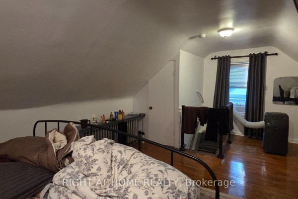 Bedroom with sloped ceiling, metal bed frame, window with dark curtains, and an air conditioner. - 179 Gilmour Avenue, Toronto