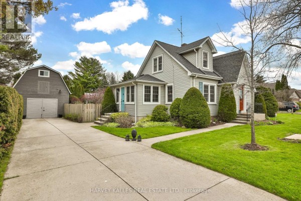 Side view of a light green house with a detached garage, concrete driveway, and green lawn. - 179 Niagara Street, Niagara On The Lake