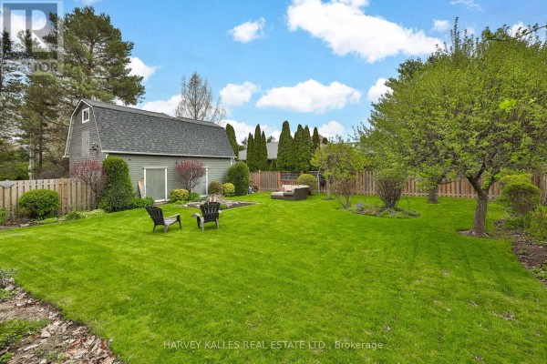 Backyard view of a green lawn with two chairs, a seating area, and a wooden fence. - 179 Niagara Street, Niagara On The Lake