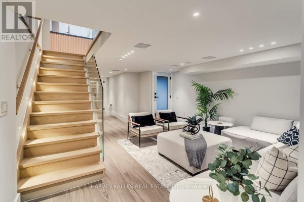 Modern living room with wood stairs and glass railing, sectional sofa, and accent chairs - 179 Palmerston Avenue Toronto