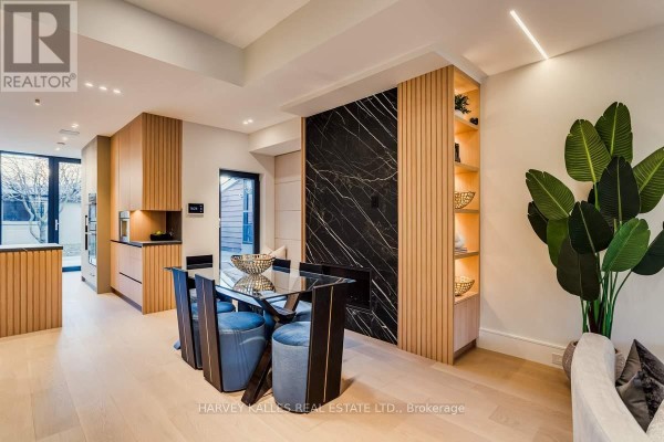 Dining area with glass table, blue chairs, marble wall, wood shelves, and kitchen. - 179 Palmerston Avenue Toronto
