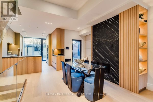 Dining area with glass table and blue chairs, adjacent to modern kitchen and marble accent wall - 179 Palmerston Avenue Toronto
