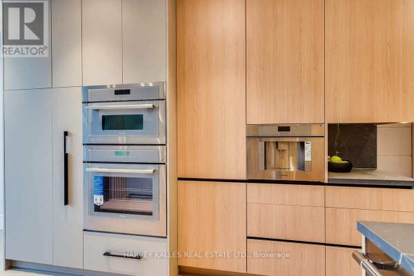 Stacked ovens, coffee maker, and wood cabinets in a modern kitchen - 179 Palmerston Avenue Toronto