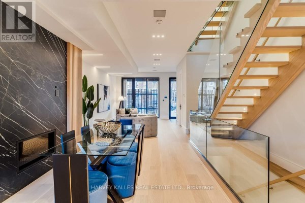 Modern dining area with glass table, velvet chairs, marble wall, fireplace & glass railing staircase - 179 Palmerston Avenue Toronto