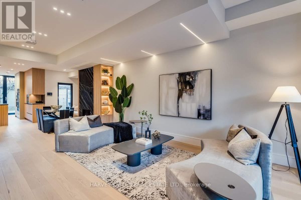 Basement living area with a sectional sofa, chairs, abstract art, and a modern glass-railed staircase. - 179 Palmerston Avenue, Toronto