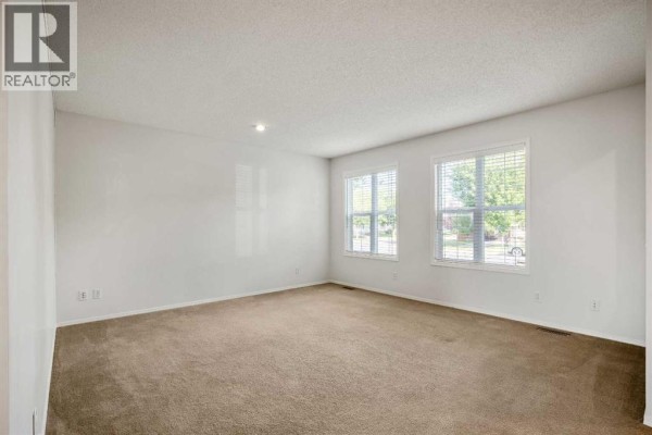 Living room with a beige sofa, two chairs, a coffee table, and a large area rug. - 179 Prestwick Drive Se, Calgary