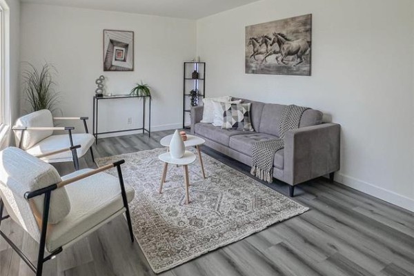Living room features a grey sofa, patterned rug, two white accent chairs, and artwork on the wall. - 1795 Manitoba Avenue, Winnipeg