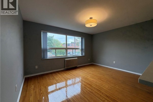 Living room with hardwood floors, grey walls, large window, and radiator. - 1797 Main Street W Unit# 18, Hamilton