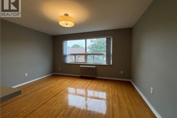 Living room showing hardwood floors, grey walls, and a large window with external view. - 1797 Main Street W Unit# 18, Hamilton