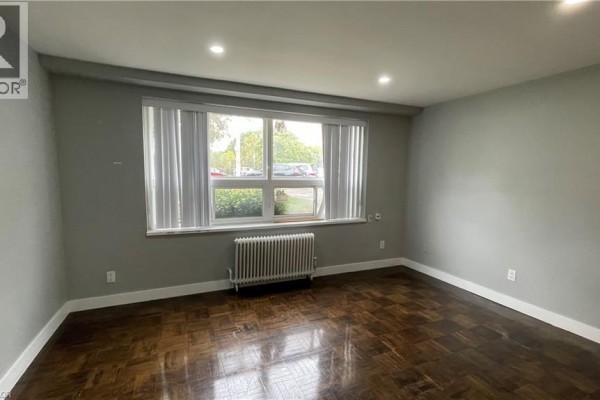 Room with dark hardwood floors, grey walls, vertical blinds, and a large window. - 1797 Main Street W Unit# 3, Hamilton