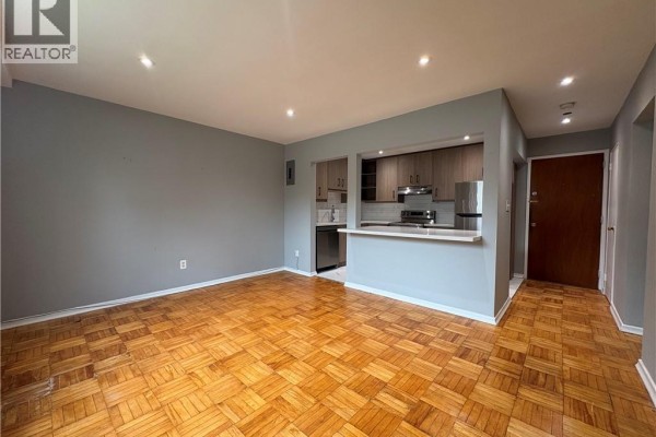 Living area with parquet flooring and a view into the open-concept kitchen with wood cabinets and stainless steel appliances. - 1797 Main Street W Unit# 4, Hamilton