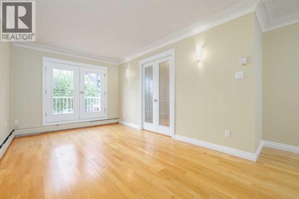 Living room with light wood floors, crown molding, and frosted glass double doors. - 18, 1813 25 Avenue Sw, Calgary