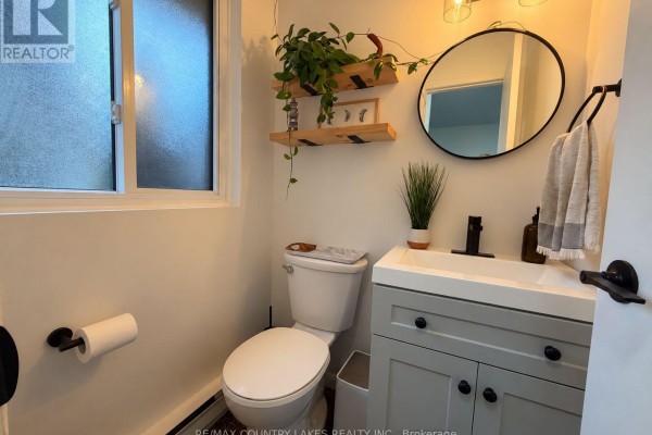 Powder room with a toilet, light grey vanity, and a round mirror on the wall. - 18 - 2 Paradise Boulevard, Ramara