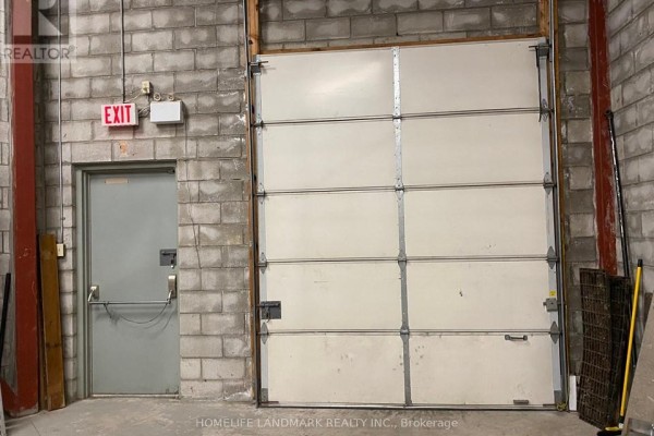 Warehouse area with a metal garage door, an exit door, and concrete block walls. - 18 - 60 West Wilmot Street, Richmond Hill
