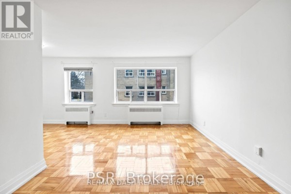 Empty room with parquet flooring and white walls, featuring two windows - 18 - 69 Old Mill Terrace, Toronto