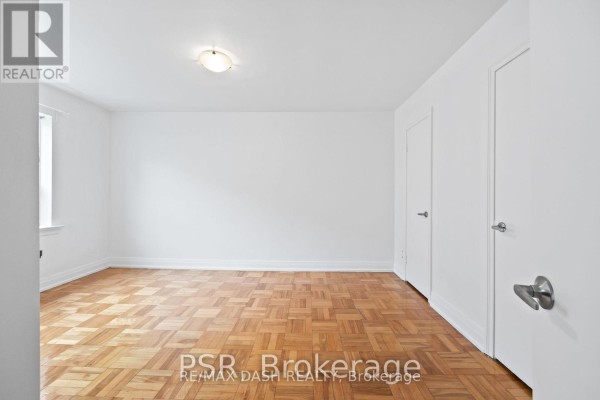 Living area with parquet flooring, two windows, and a view of the hallway - 18 - 69 Old Mill Terrace, Toronto