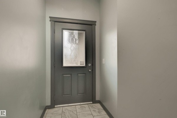 View of the kitchen showing grey cabinets, a refrigerator, and a doorway to another room. - #18 4900 62 St, Beaumont