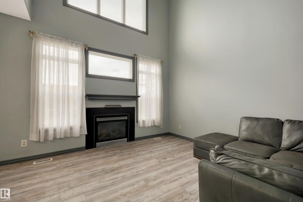 Corner view of the living room with a sectional sofa, a decorative clock, and a staircase with a dark metal railing. - #18 4900 62 St, Beaumont