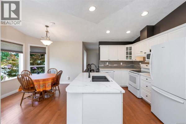 Kitchen and dining area with white cabinets, island, pendant light, and wooden table. - 18 6000 St. Ann's Dr, Duncan