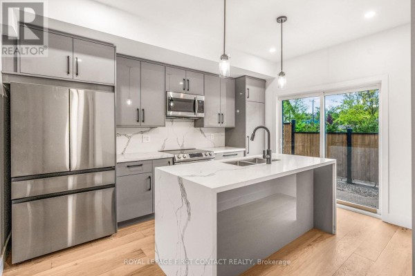 Kitchen with grey cabinets, island, stainless steel appliances, and sliding glass doors to the backyard. - 18 Alderwood Lane, Barrie