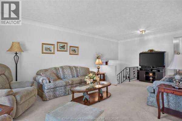 Living room with beige carpet, floral sofas, armchairs, television, and a staircase. - 18 Cameo Drive, Leamington