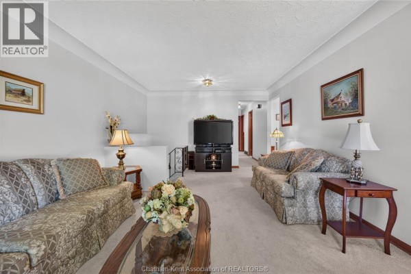 Living room with beige carpet, floral sofas, armchairs, and a television on a stand. - 18 Cameo Drive, Leamington