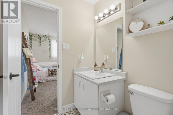 Bathroom vanity, sink, mirror, toilet, and shelving visible. Bedroom with bed and ladder to the left - 18 Chapman Court London North